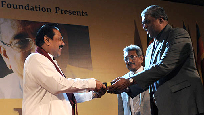 Sri Lankan journalist C.A Chandraprema (R) gives a copy of 'Gota's War' to Sri Lankan President Mahinda Rajapakse (L) as defence secretary Gotabhaya Rajapaksa looks on during the launch of the book 'Gota's War' in Colombo on May 14, 2012.  'Gota's War' looks back at the successful military campaign against the Tamil Tiger rebels and the role played by Gotabhaya Rajapaksa, the younger brother of the president. AFP PHOTO/Ishara S. KODIKARA        (Photo credit should read Ishara S.KODIKARA/AFP/GettyImages)