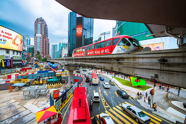 Kuala Lumpur, Malaysia - April 10, 2015: Downtown Kuala Lumpur crossing with road, train and billboards. Cars and a monorail car rush through the Bukit Bintang intersection.